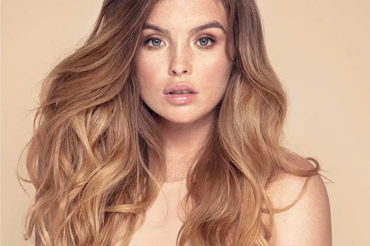 Mujer con cabello largo y ondulado, con un balayage inverso que va de castaño oscuro a rubio miel.