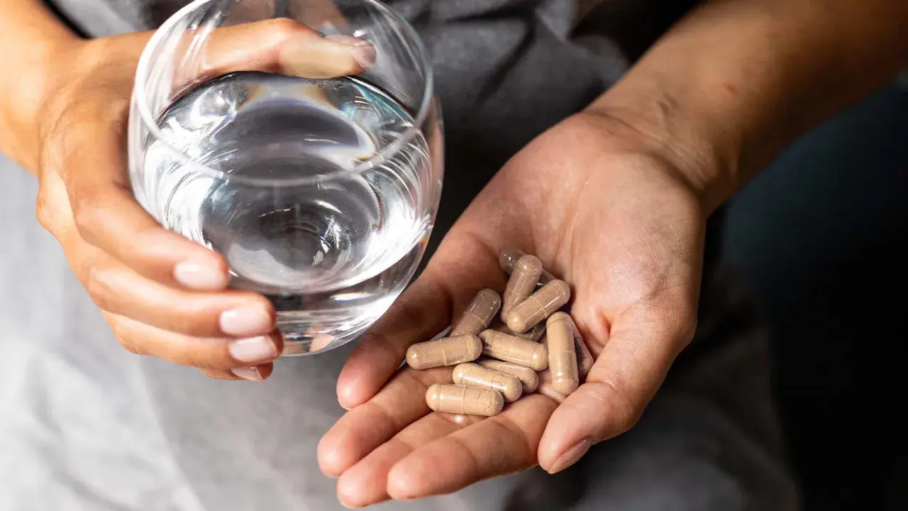 Manos sostienen un vaso de agua y cápsulas, ilustrando cómo tomar probióticos con antibióticos para el bienestar intestinal.