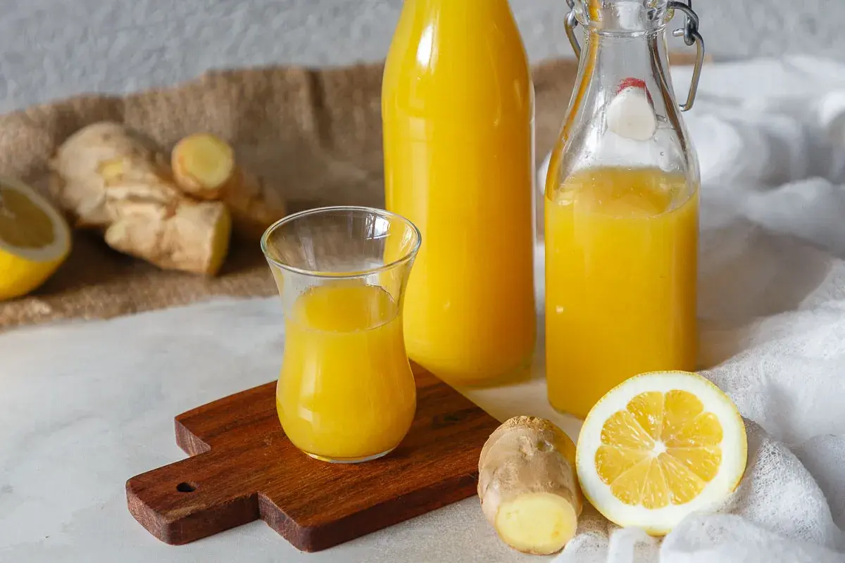 Ingwerwasser kochen oder nicht? Frischer Ingwer, Zitrone und goldgelbes Ingwerwasser in Flaschen und Glas.