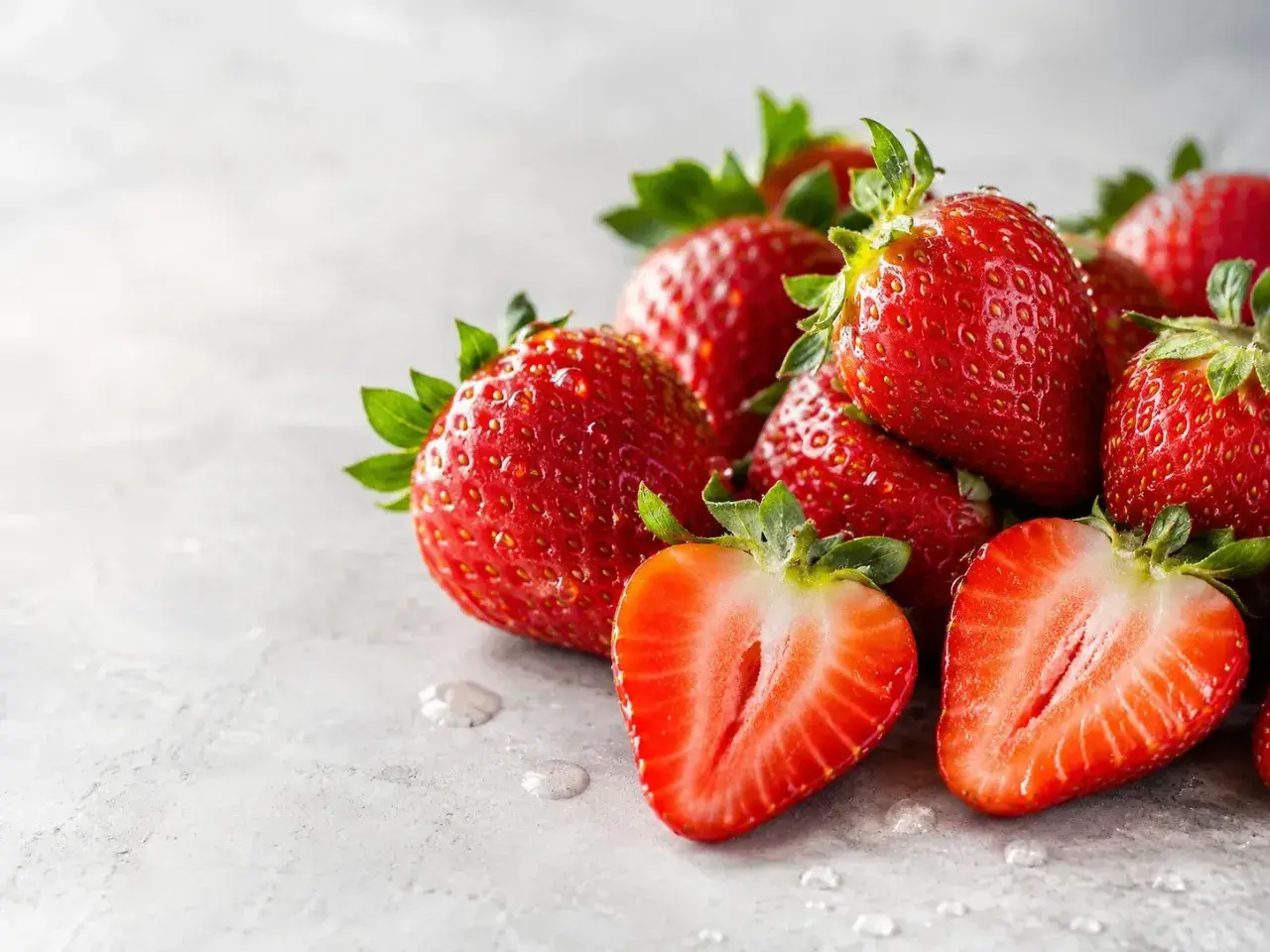Fragole succose, ricche di potassio, su sfondo grigio. Una tagliata rivela la polpa rossa e i semini.