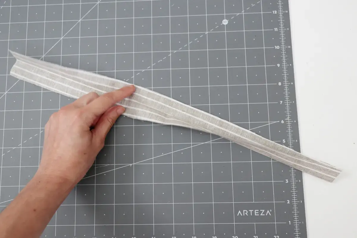 A hand points to a striped fabric strip, possibly for a belt loop pattern, on a cutting mat.