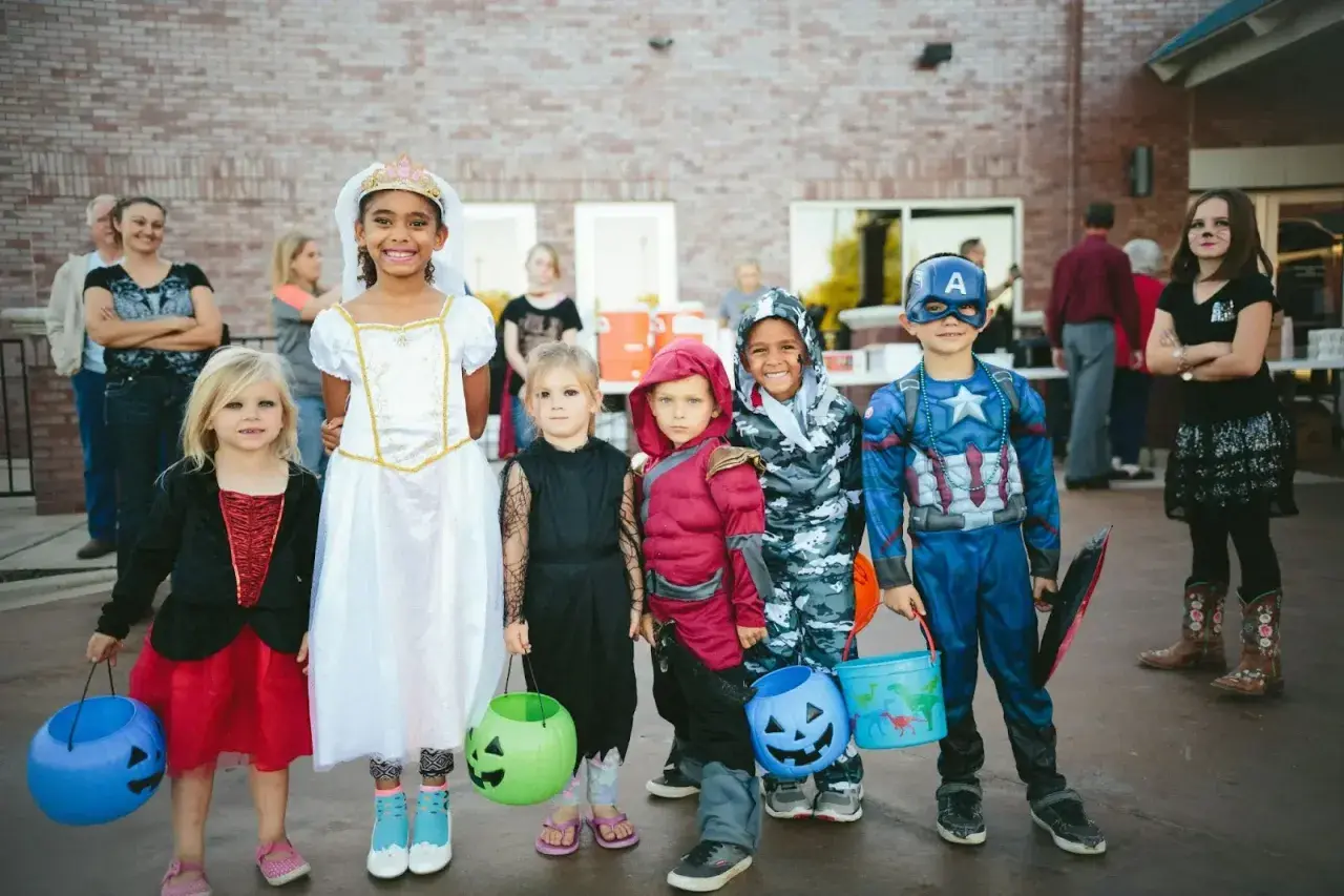 Dzieci w strojach na Halloween, gotowe na psikusy i zbieranie słodyczy. Wśród nich księżniczka, Kapitan Ameryka i inne postacie.