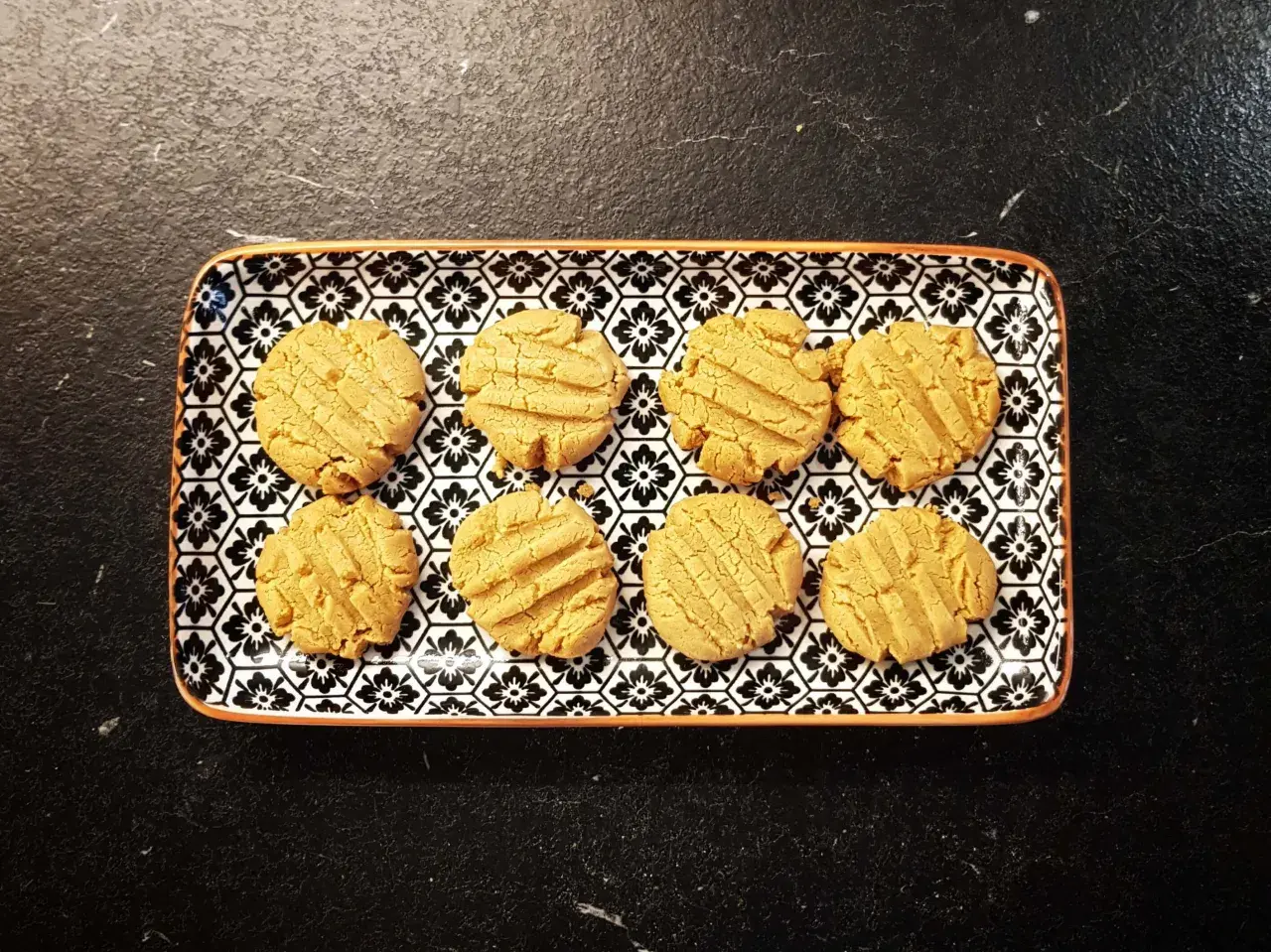 A rectangular plate with a black and white floral pattern holds eight golden-brown kekse ohne zucker.