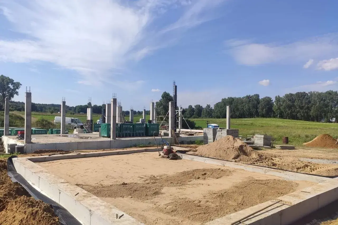 Budowa domu w toku. Widać fundamenty, betonowe słupy i hałdy piasku, który czeka na zagęszczenie.