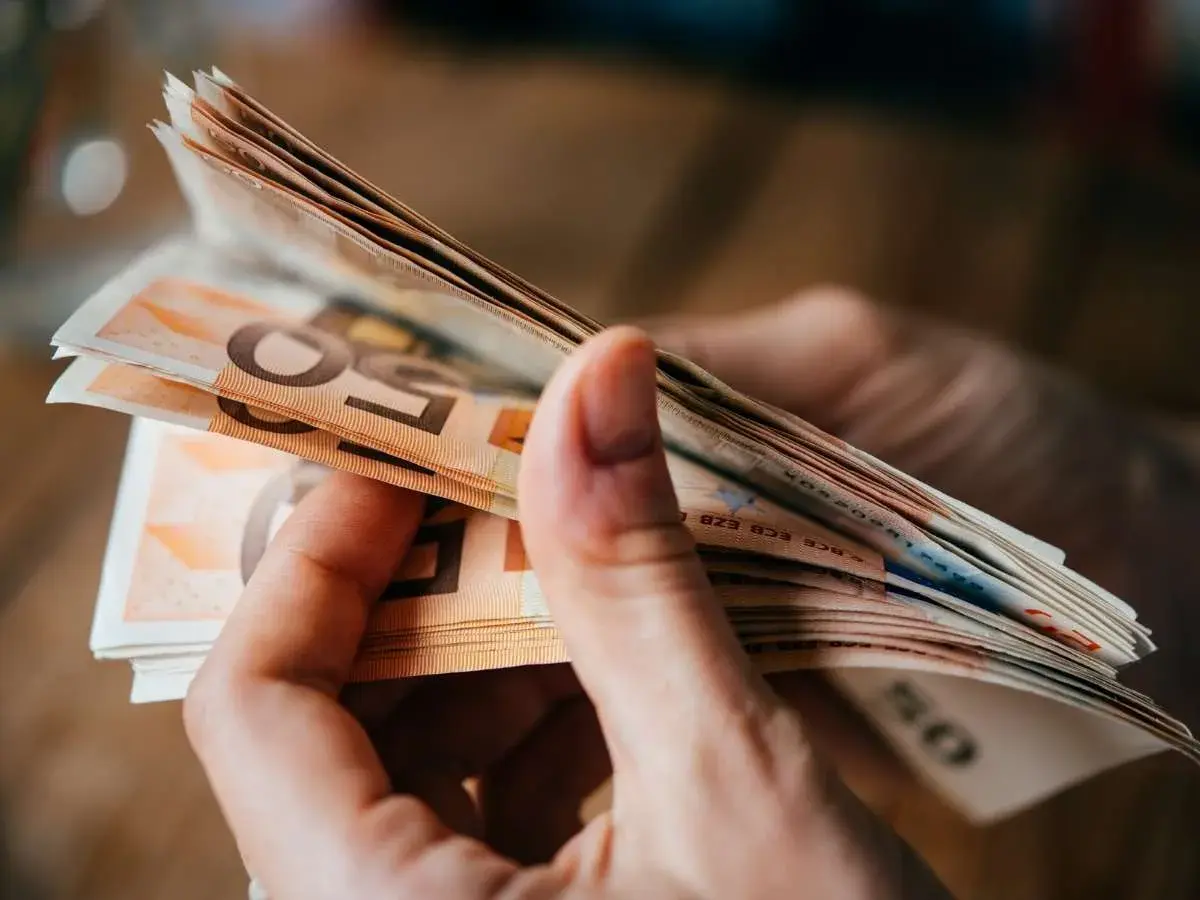 Hände halten einen Stapel Euro-Scheine. Dies könnte relevant sein für den **privatinsolvenz freibetrag**.
