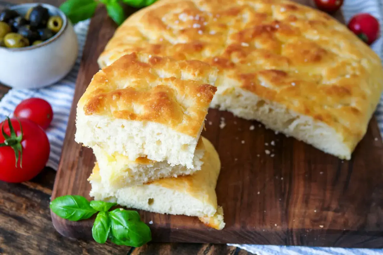 Frisch gebackene Focaccia, ein köstliches original focaccia rezept, mit Tomaten, Oliven und Basilikum auf einem Holzbrett.