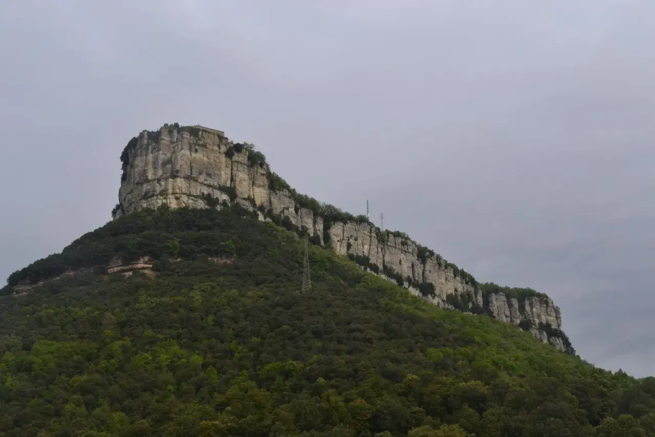 Imponent roca amb vegetació verda i una construcció al cim, recordant la Mare de Déu del Far.