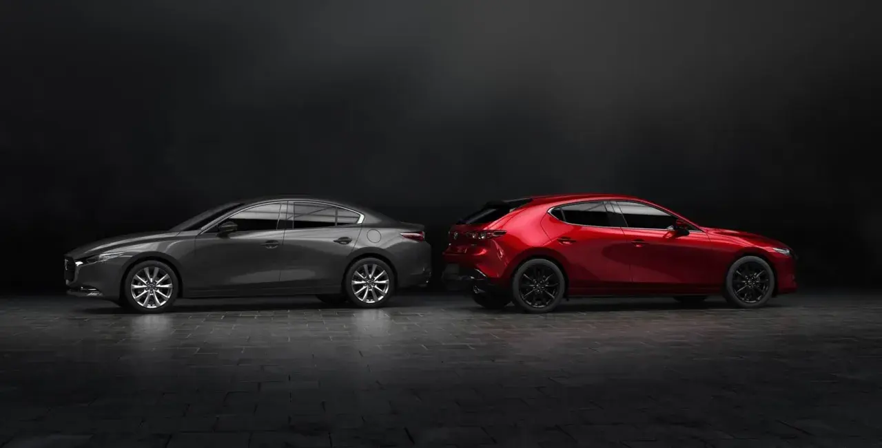 Szary sedan Mazda 3 i czerwony hatchback stoją obok siebie na ciemnym tle.