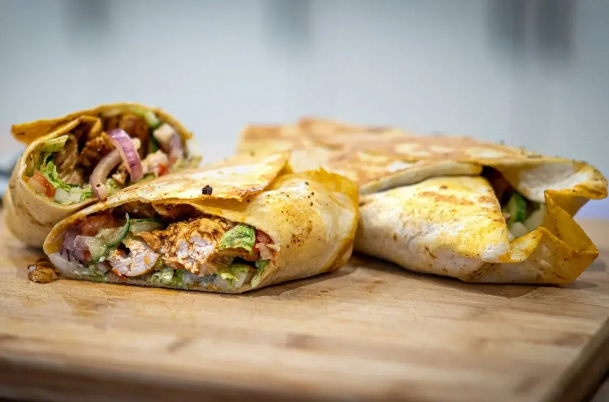 Pyszny kebab w tortilli z kurczakiem, warzywami i cebulą, ułożony na desce.