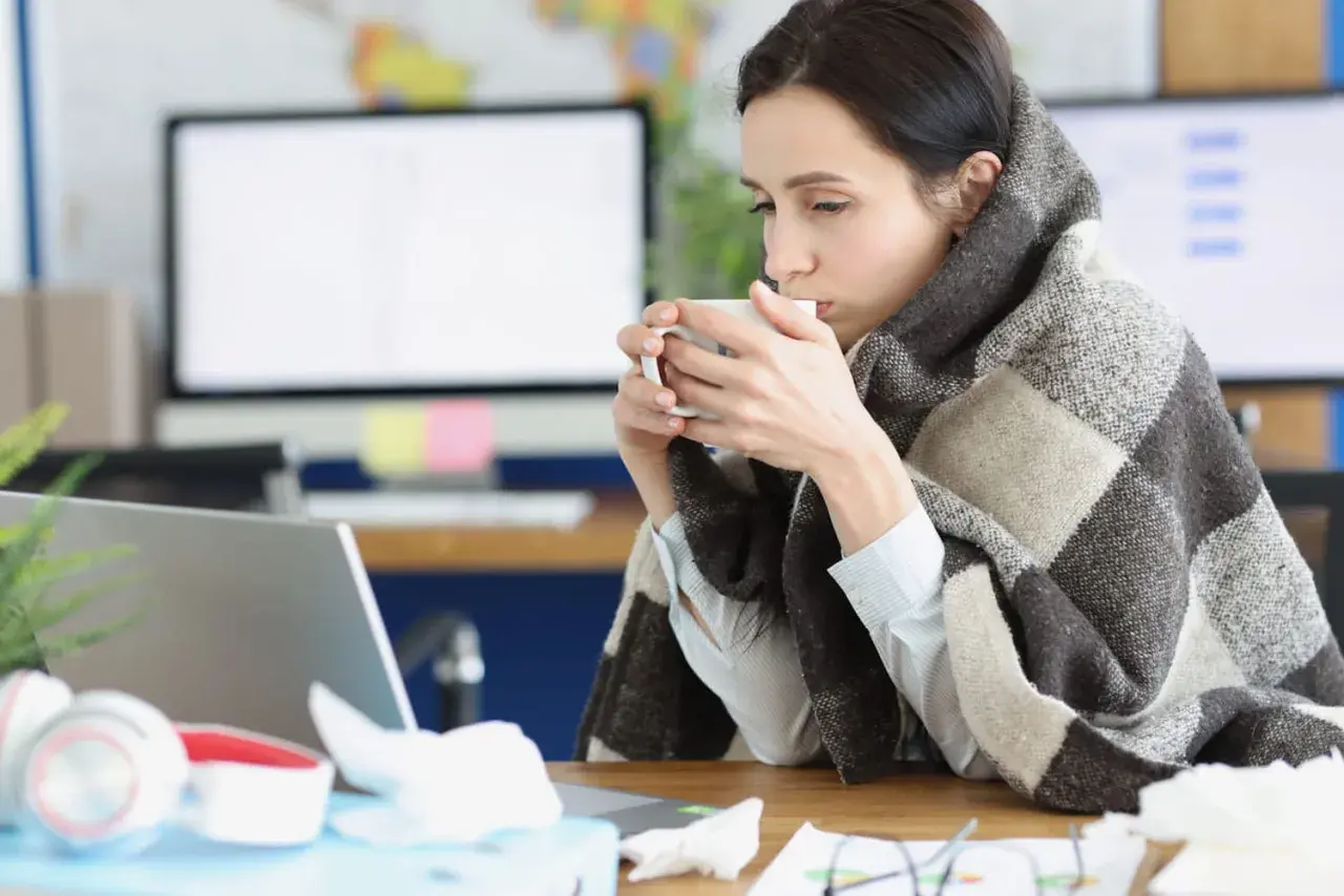 Femme emmitouflée dans une couverture, buvant une tasse de thé, peut-être à cause d'une mauvaise température ambiente.