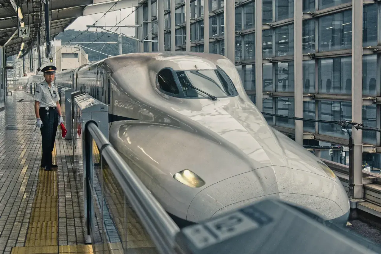 Na peronie stoi konduktor obok najszybszej kolejki na świecie, Shinkansen, gotowej do podróży.