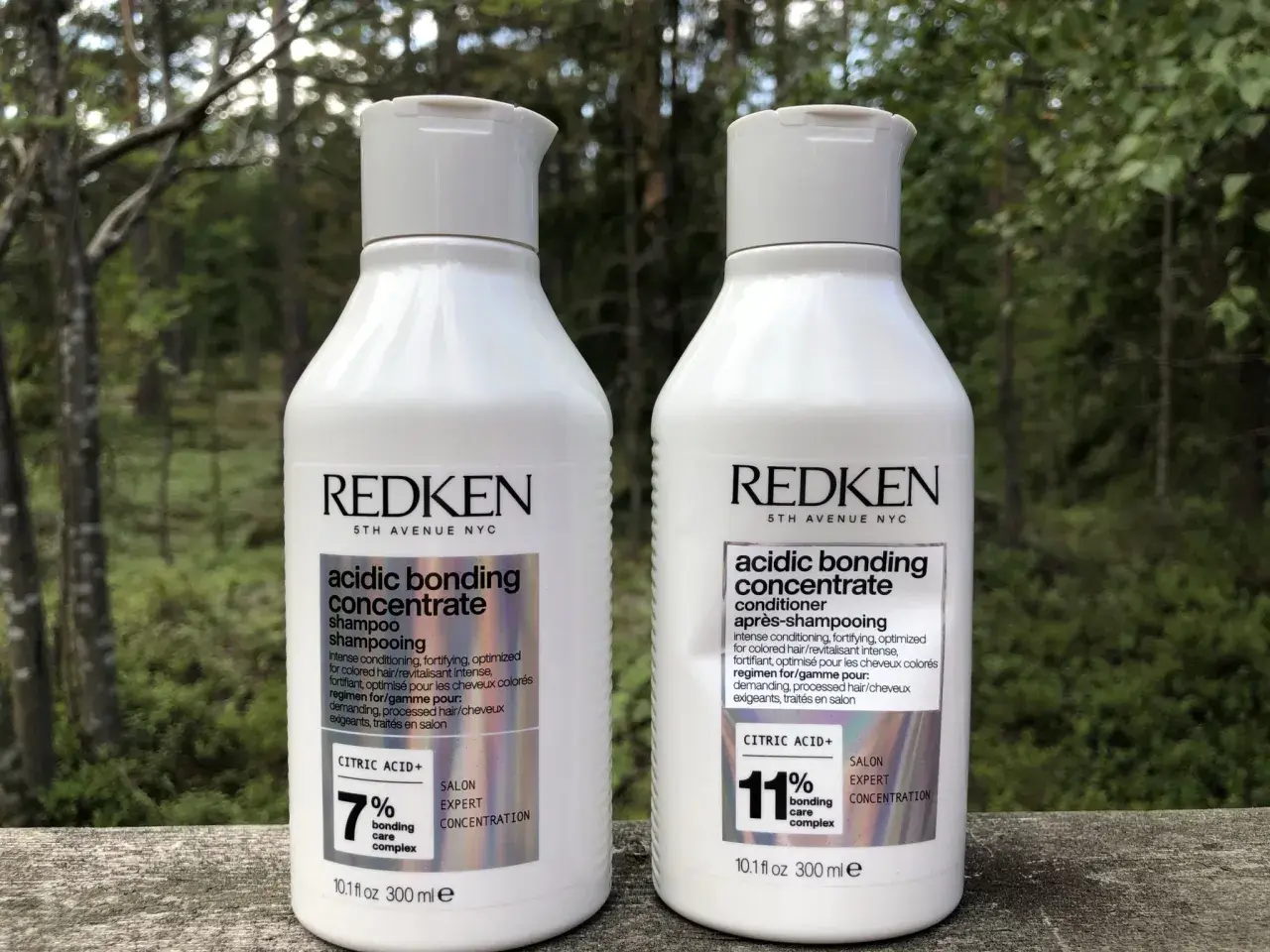 Två flaskor Redken Acidic Bonding Concentrate, schampo och balsam, står utomhus. Perfekt för att reparera skadat hår efter färgning.