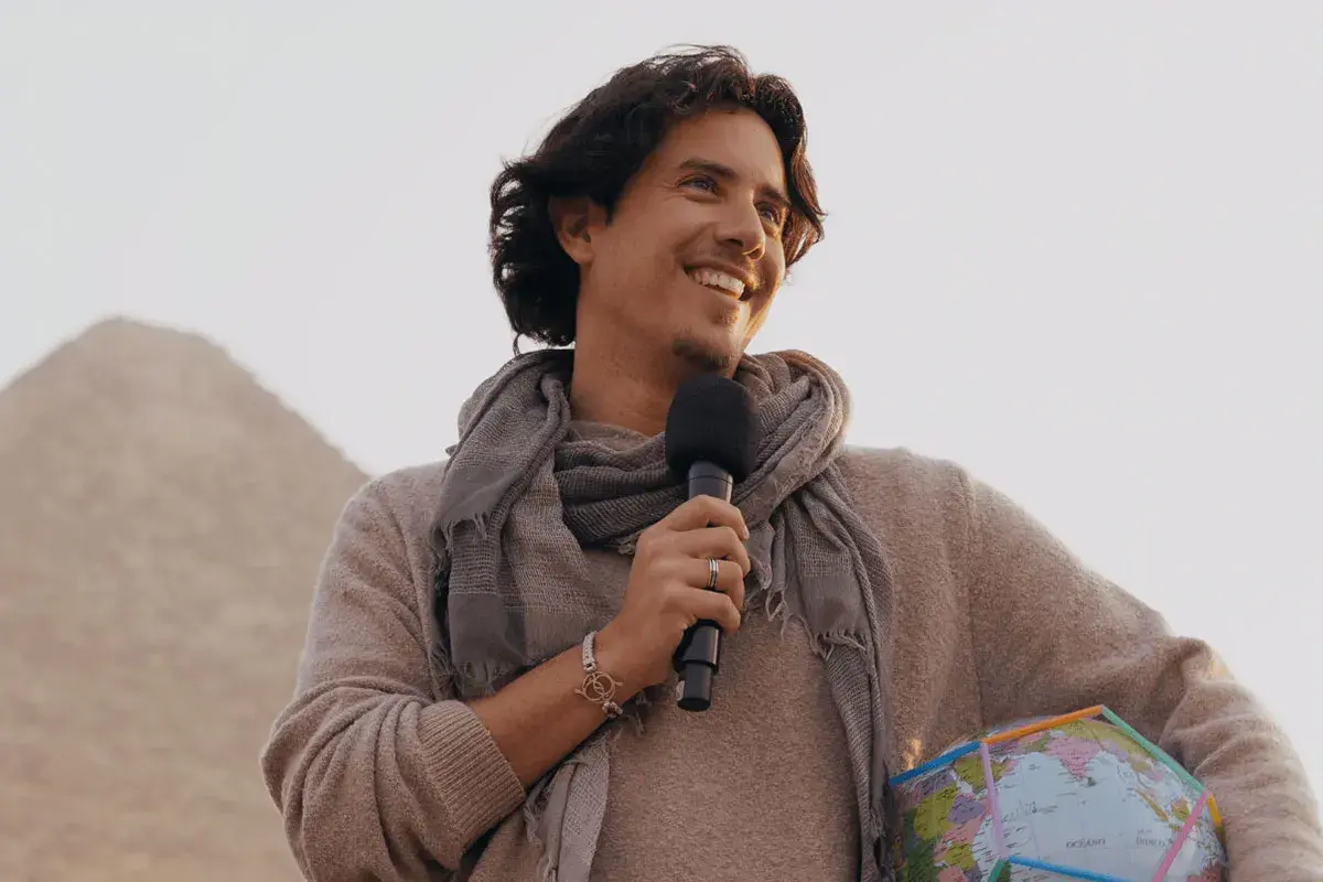 Matias de Stefano, con un micrófono y un globo terráqueo, sonríe ante una pirámide.