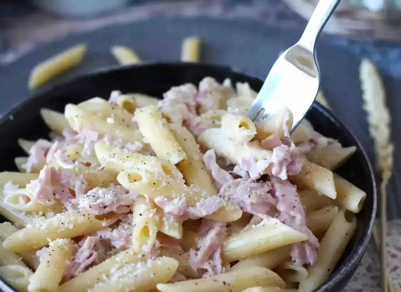 En gaffel lyfter en tugga av krämig skinksås pasta, toppad med riven ost och svartpeppar.