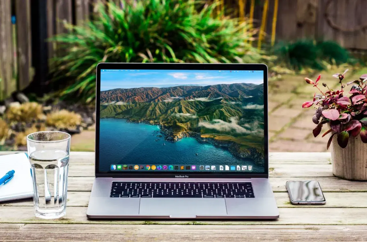MacBook Pro z widokiem na wybrzeże Kalifornii. Obok szklanka wody, notatnik i telefon. Wiele marek laptopów oferuje podobne możliwości.