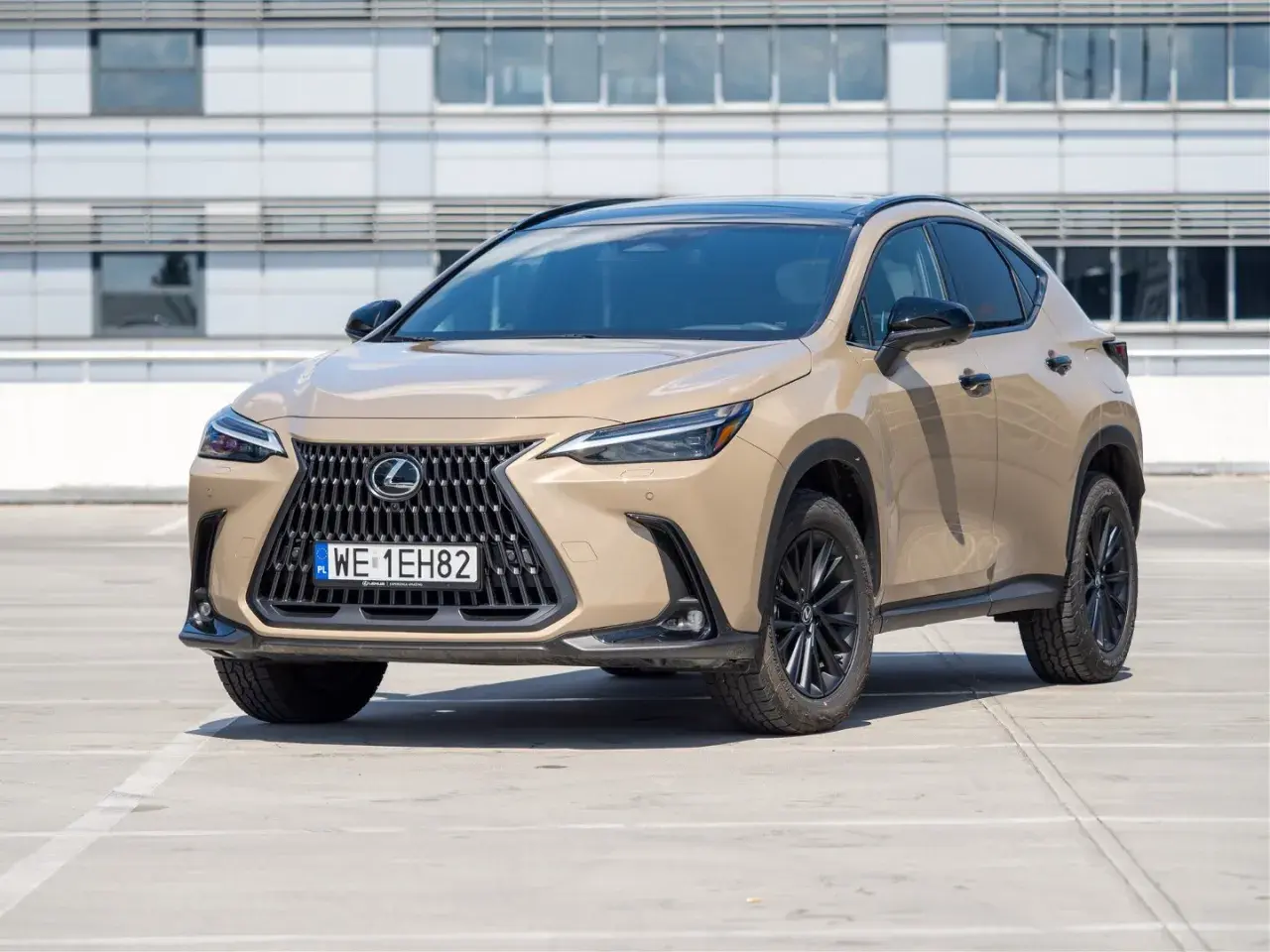 Elegancki, beżowy Lexus 350h z czarnym dachem i felgami stoi na parkingu przed nowoczesnym budynkiem.