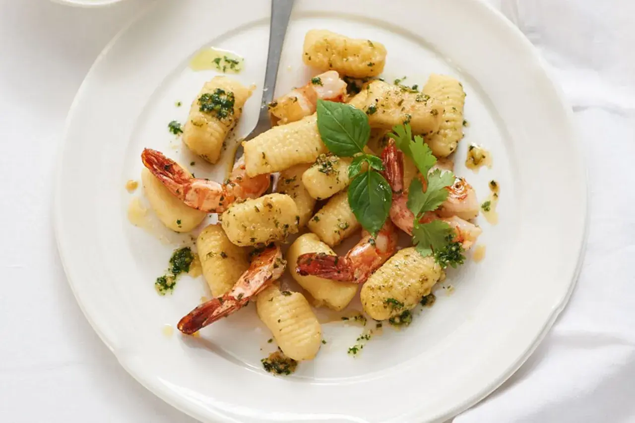 Gnocchi mit Garnelen, verfeinert mit Kräutern und Öl, auf einem weißen Teller angerichtet.