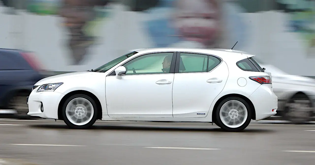 Biały Lexus CT200h w ruchu ulicznym, z rozmytym tłem i innymi samochodami.