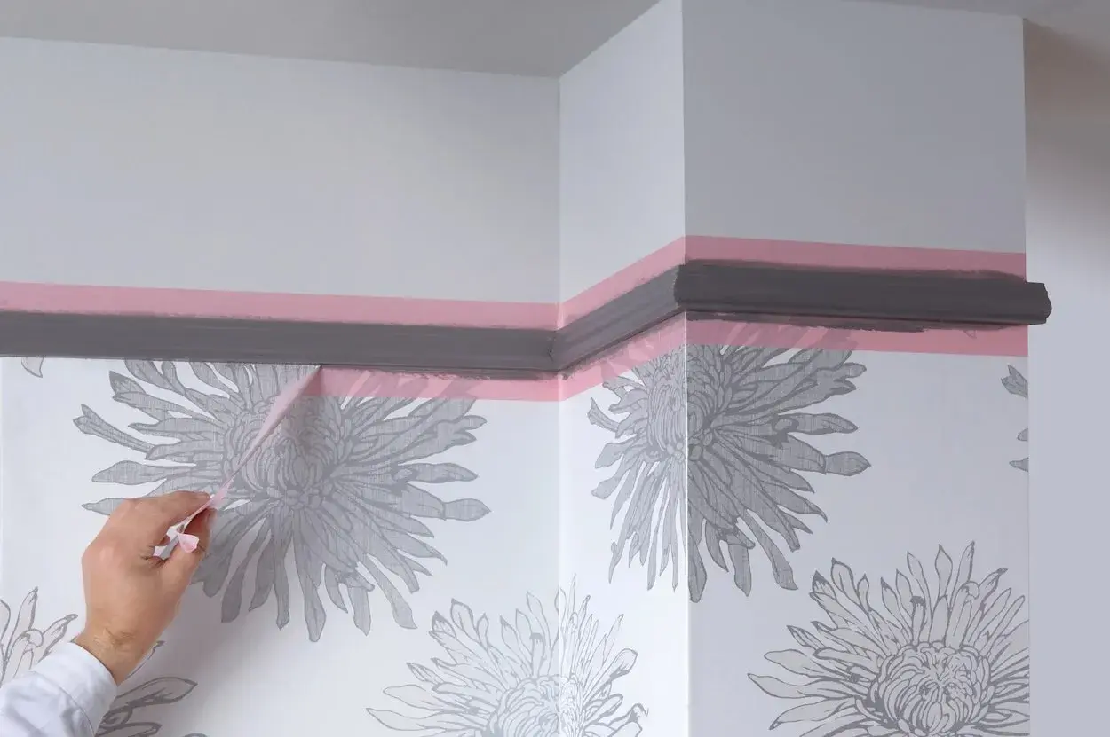 Maintenant, quand enlever bande cache peinture pour une finition parfaite. Un coin de mur avec papier peint à fleurs grises et moulure peinte en gris.