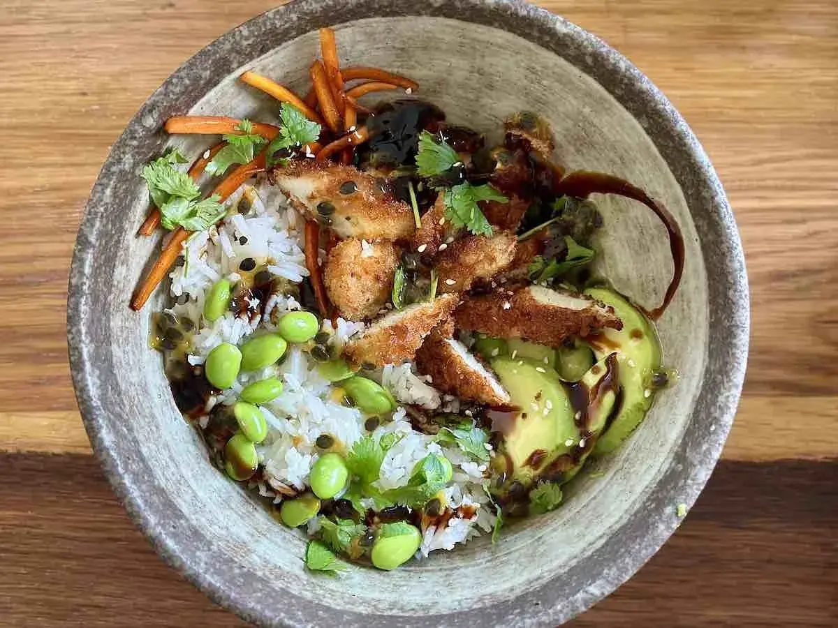 Apetyczny bowl z kurczakiem w panierce, ryżem, awokado, edamame i słodko-kwaśnym sosem.