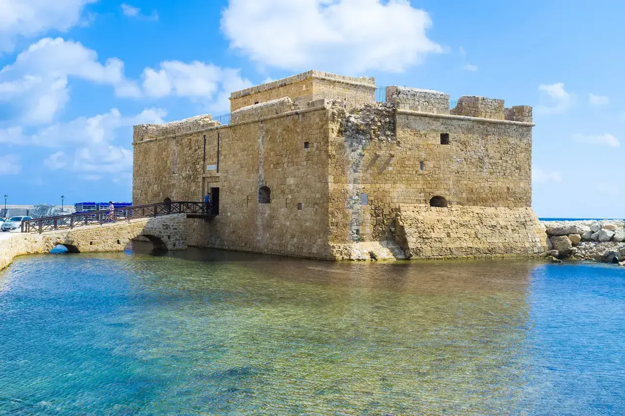 Zamek w Pafos, kamienna twierdza nad turkusową wodą, z mostem prowadzącym do wejścia.