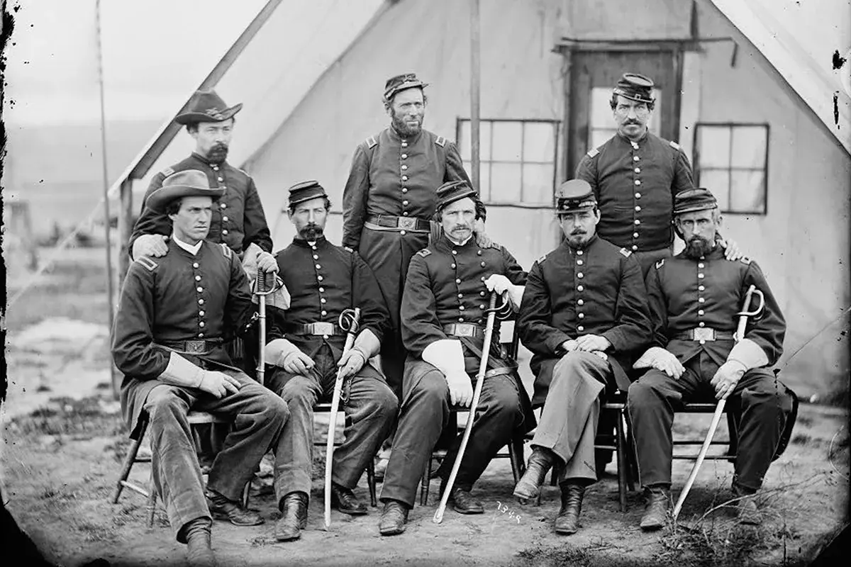 Gruppbild av nio män i uniformer från amerikanska inbördeskriget. De sitter och står framför ett tält. En enhetlig serie av militärkläder.