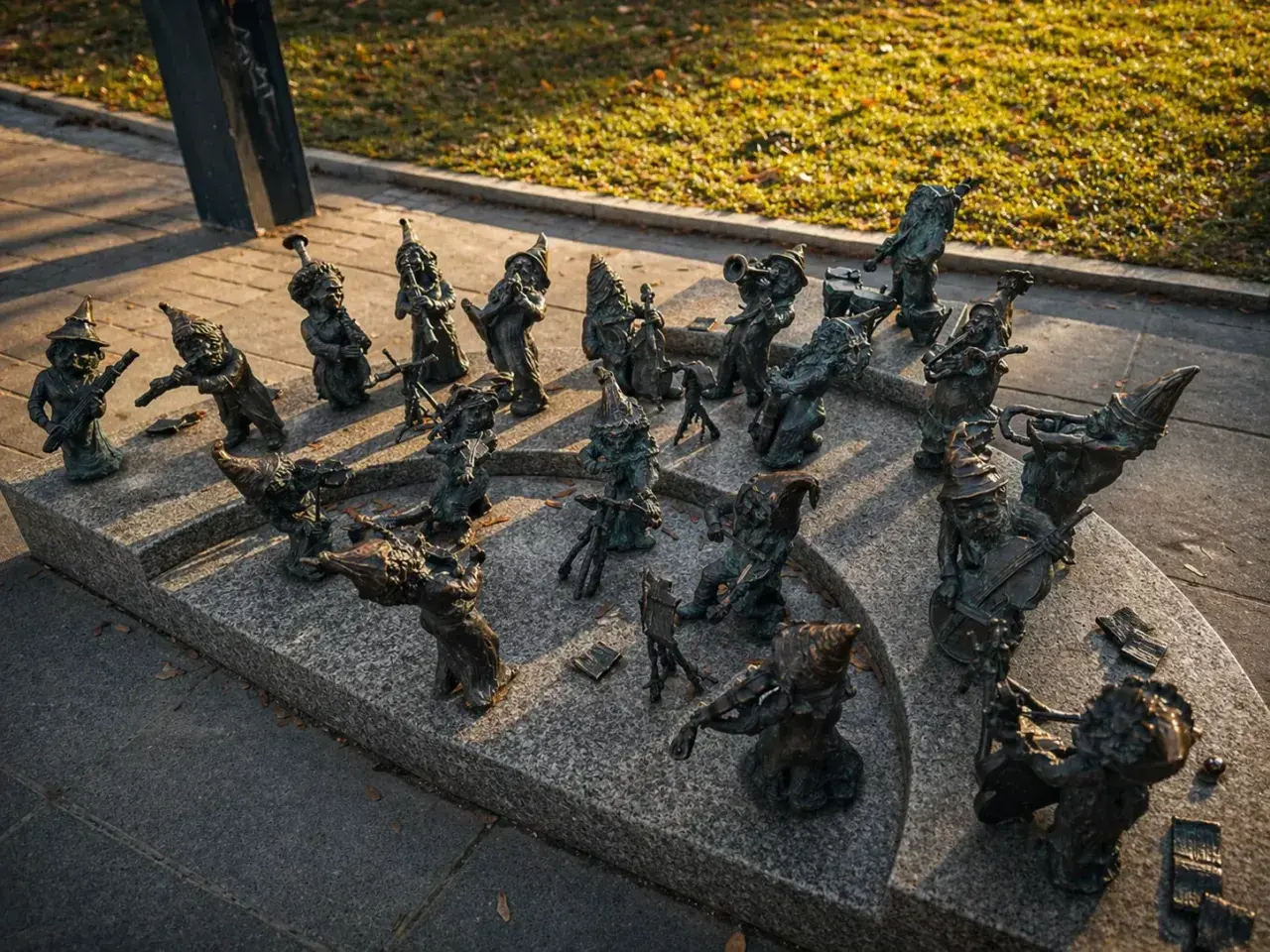 Wrocławskie krasnale, muzycy z brązu, grają na instrumentach na kamiennym postumencie.