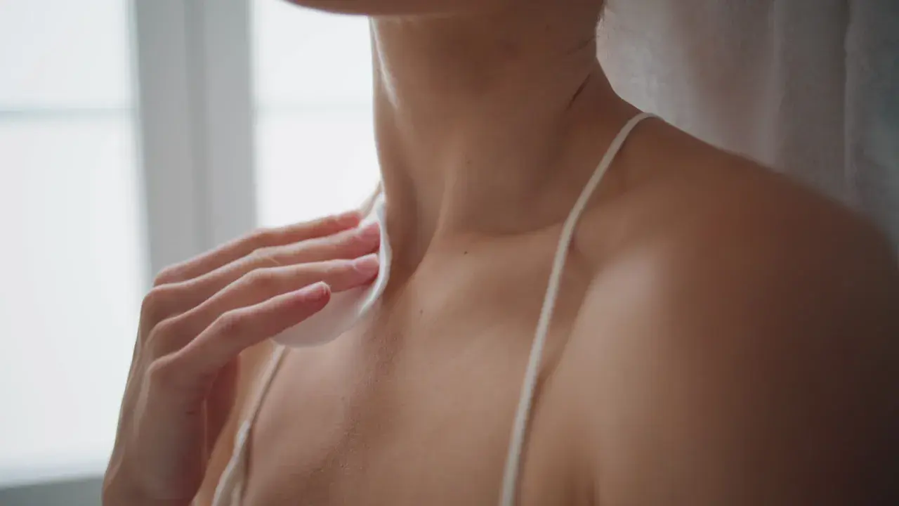A hand holds a cotton pad to a person's neck and shoulder area.