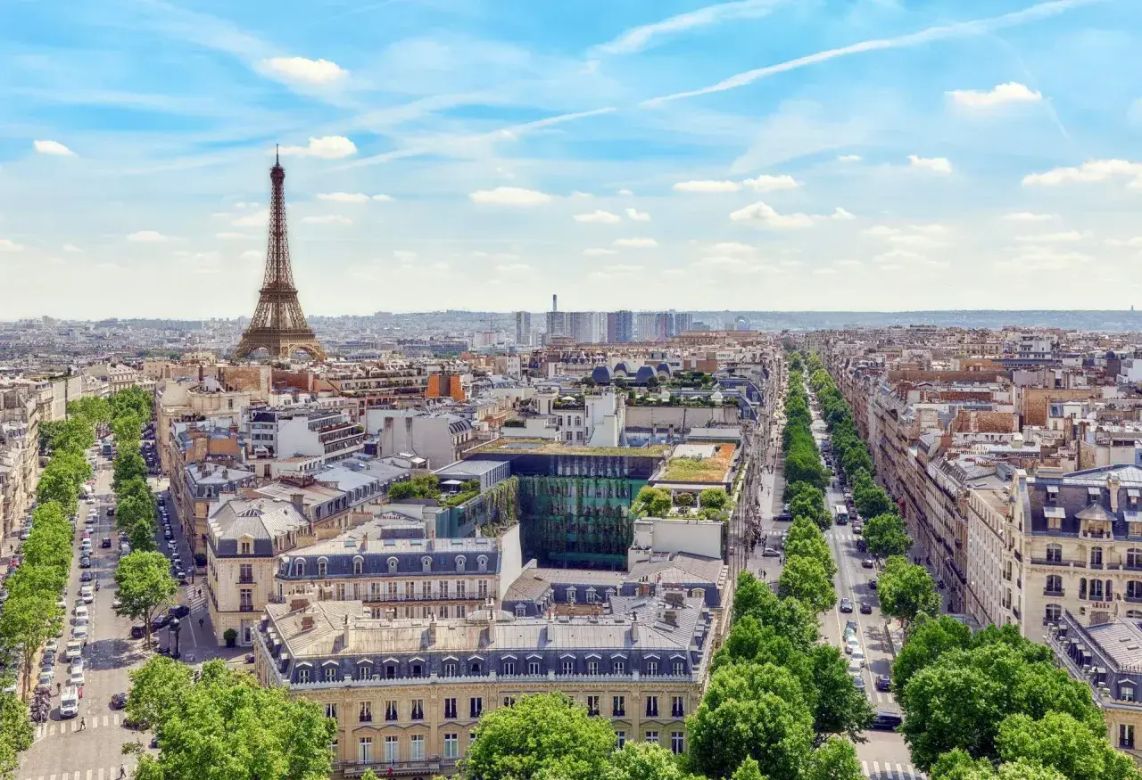 Vy över Paris med Eiffeltornet i fjärran. En grönskande allé leder mot stadens centrum, där takåsarna vittnar om stadens rika historia och många museum.