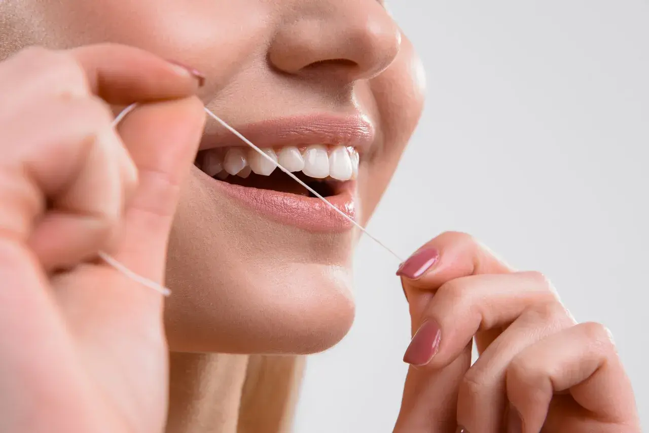 Primo piano di una donna che usa il filo interdentale per pulire i denti. Impara scovolino denti come si usa per un sorriso smagliante.