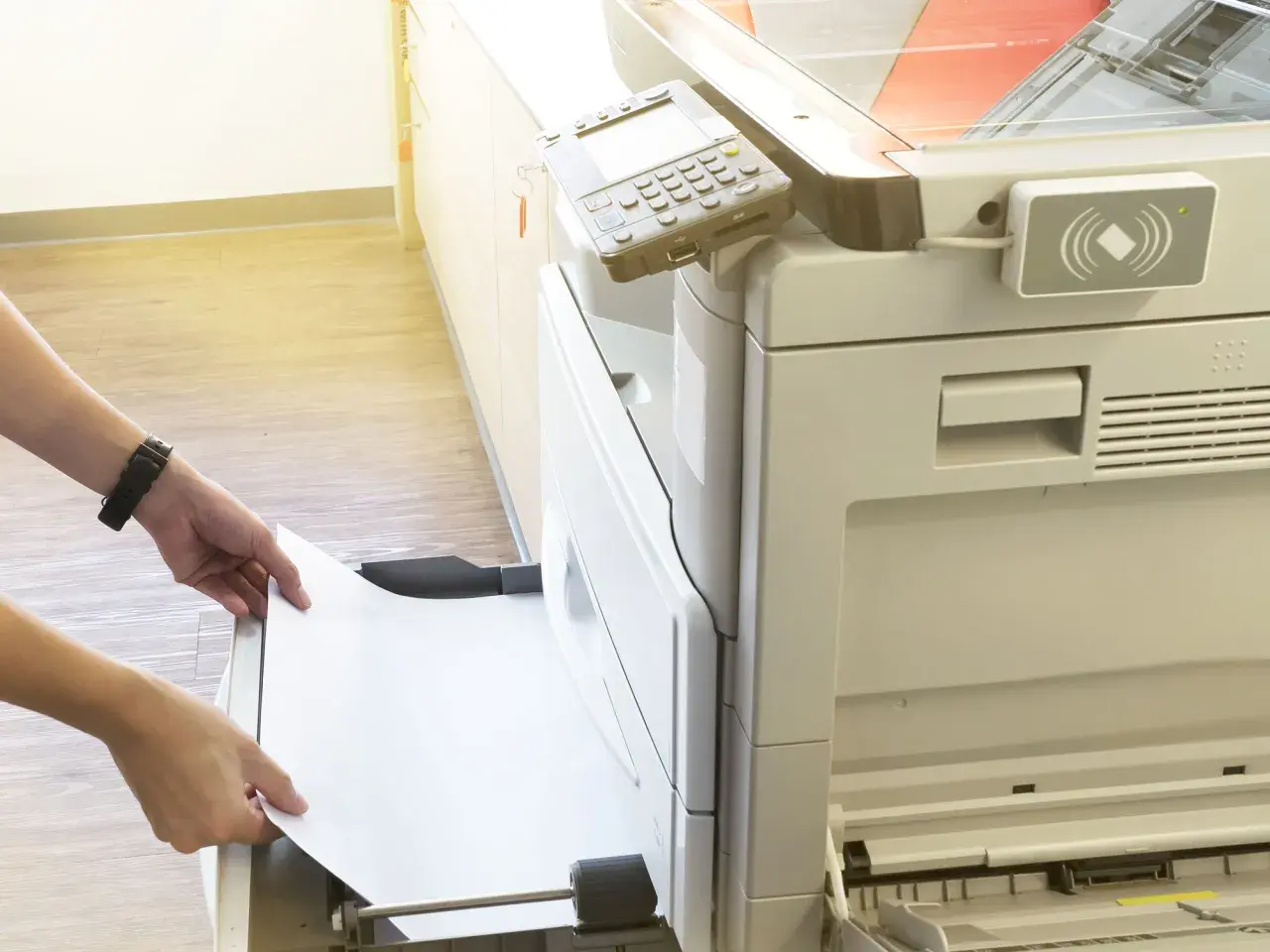 Mani inseriscono un foglio di carta in una stampante, pronta per stampare in formato super A3.