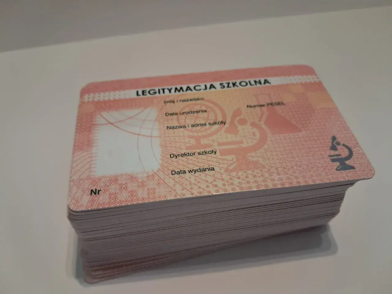 Stos nowych legitymacji szkolnych z widocznym napisem "LEGITYMACJA SZKOLNA" i mikroskopem.