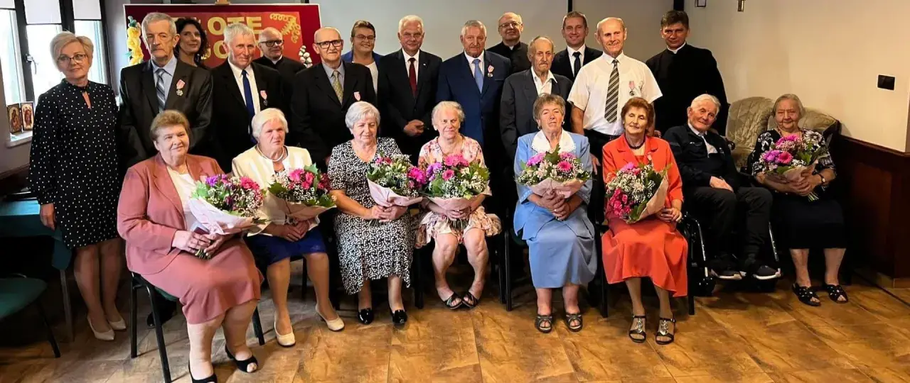 Uroczystość z okazji złotych godów. Seniorzy z bukietami kwiatów świętują 50 lat małżeństwa.