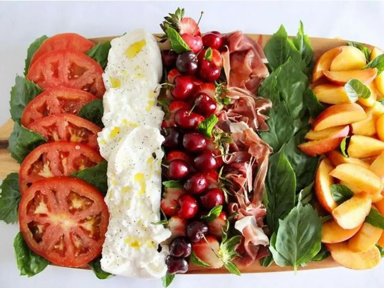 Burrata Antipasti: Tomaten, Burrata, Kirschen, Erdbeeren, Schinken und Pfirsiche auf einem Holzbrett.