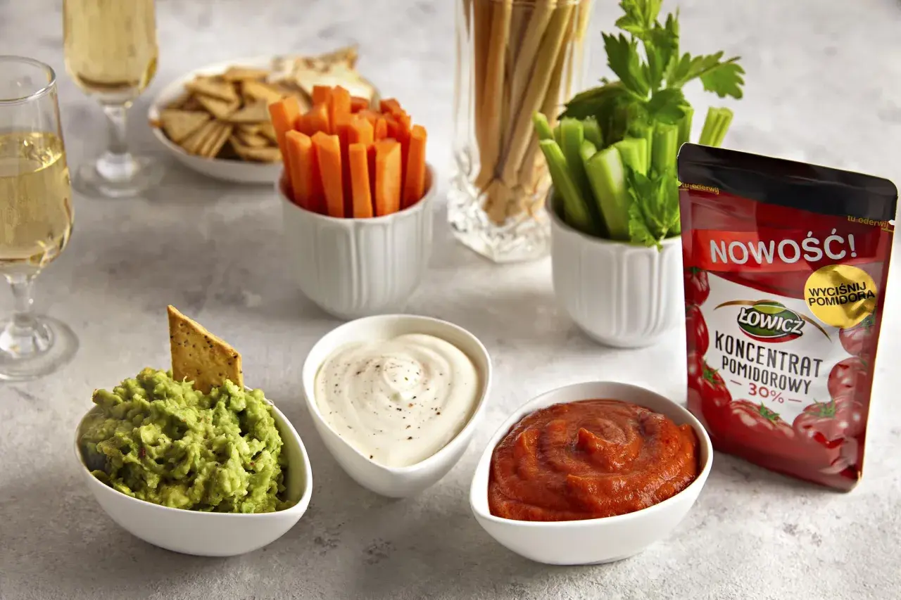 Trzy miseczki z dipami: guacamole, śmietanowym i pomidorowym, obok warzyw i krakersów.