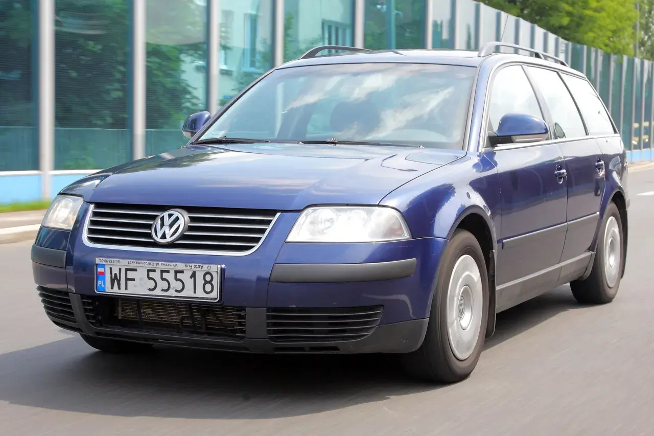 Granatowy Volkswagen Passat kombi, model b5, jedzie po drodze.