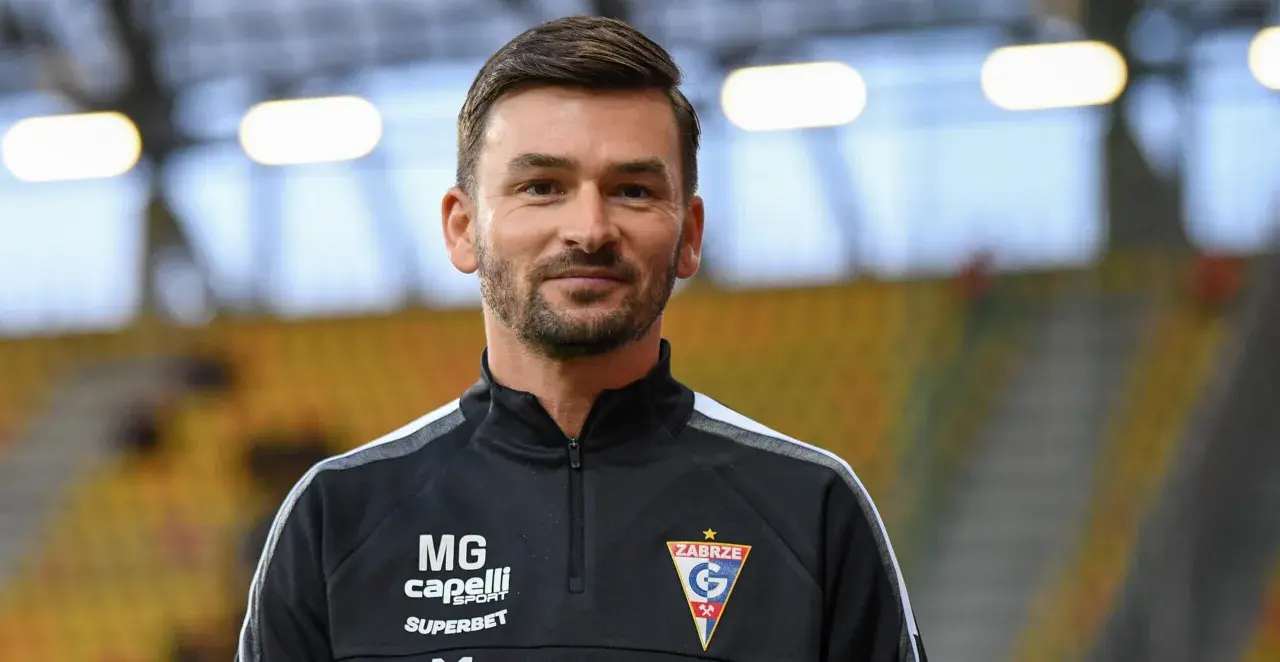 Uśmiechnięty trener Górnika Zabrze w czarnej bluzie z logo klubu.