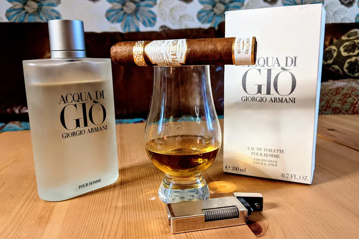 Flakon Acqua di Gio EDT, szklanka z bursztynowym płynem, cygaro i zapalniczka tworzą męski zestaw.
