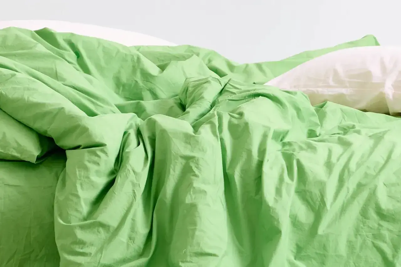 Ein Bett mit zerknitterter, leuchtend grüner Bettwäsche und einem weißen Kissen. Was ist Modal? Es ist ein Stoff, der sich so weich anfühlt.