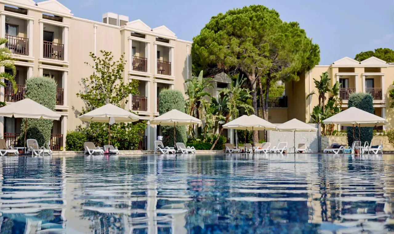 Ein Pool mit Liegen und Sonnenschirmen vor einem Hotelgebäude. Hier beginnt das magic life Belek.