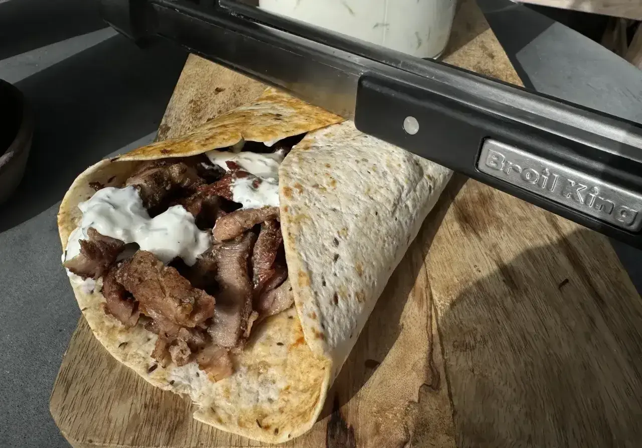Pyszny kebab kryspinów z jakim sosem, gotowy do podania. Mięso soczyste, zawinięte w tortillę, polane białym sosem.