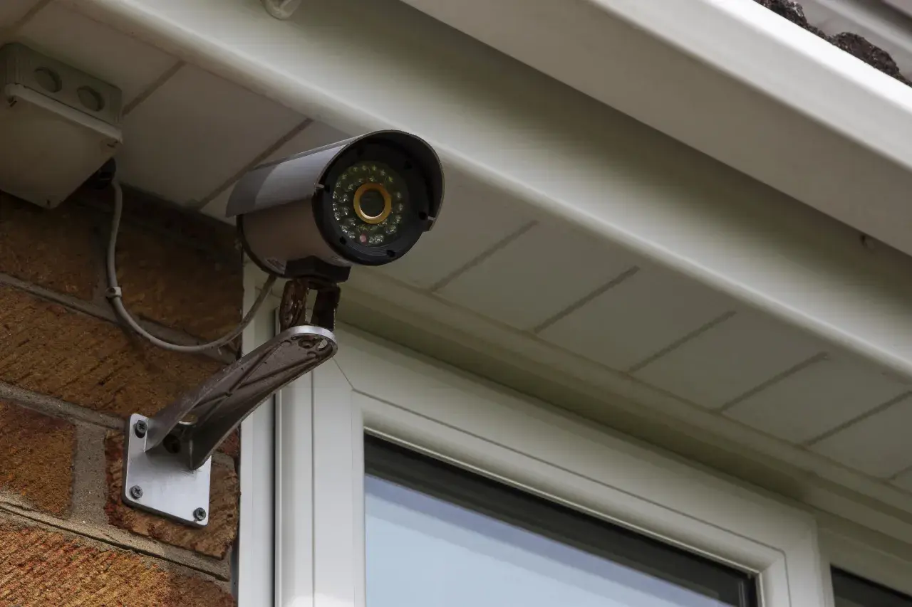 Telecamera di sicurezza, parte di un impianto di videosorveglianza, montata su una parete di mattoni sotto una grondaia.