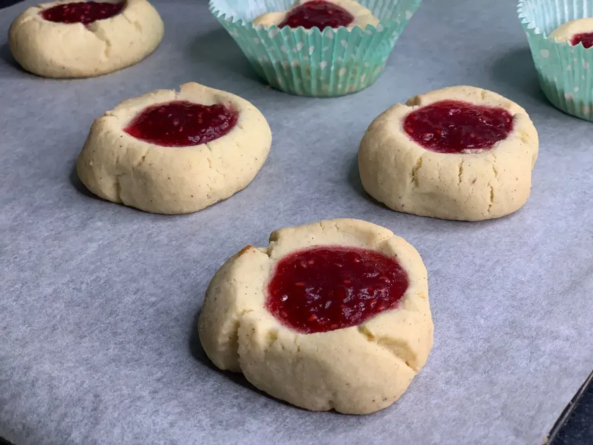Nybakade glutenfria hallongrottor med sylt på bakplåtspapper. Perfekt fika!