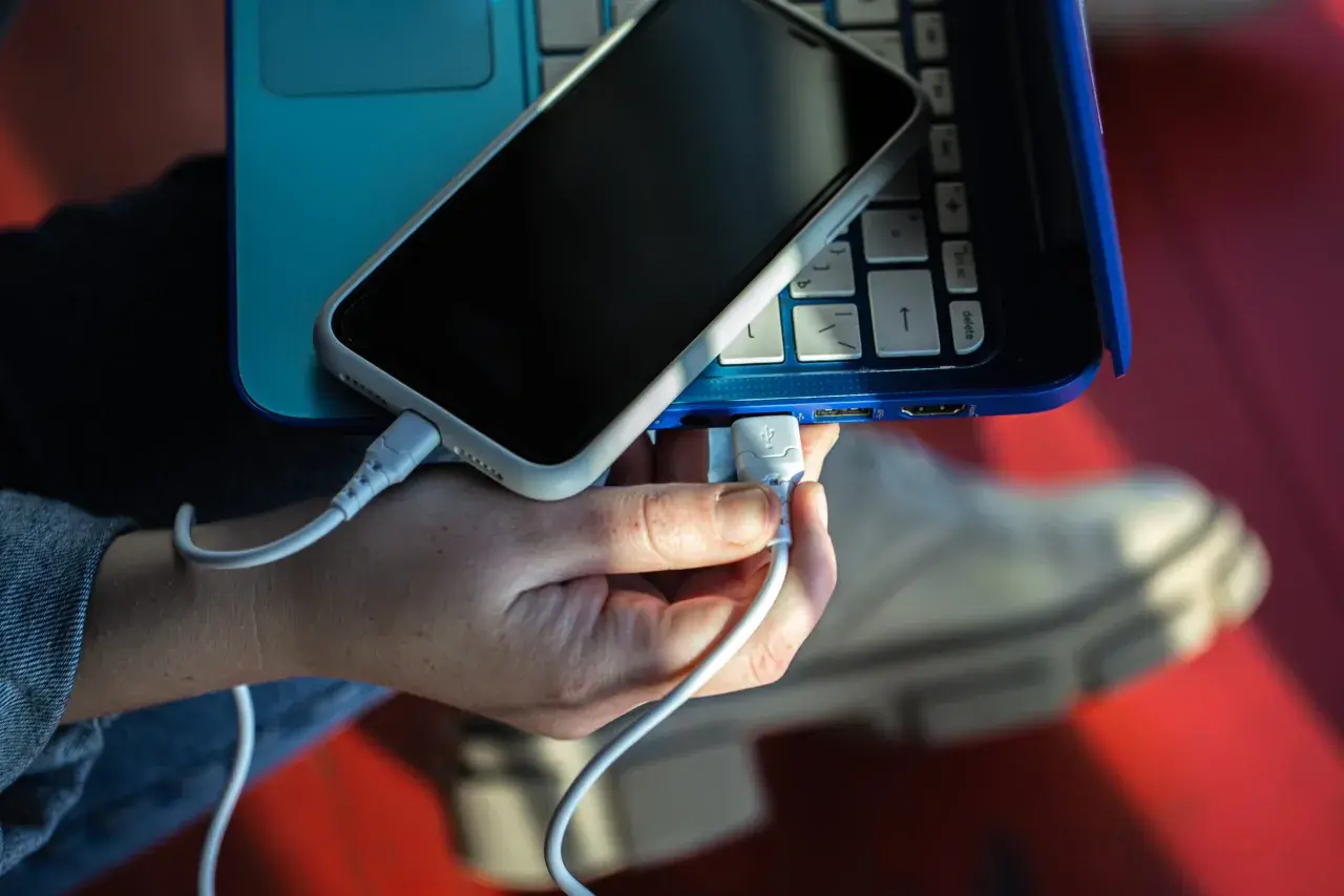 Dłoń podłącza kabel USB telefonu do laptopa, pokazując, jak połączyć telefon z laptopem.