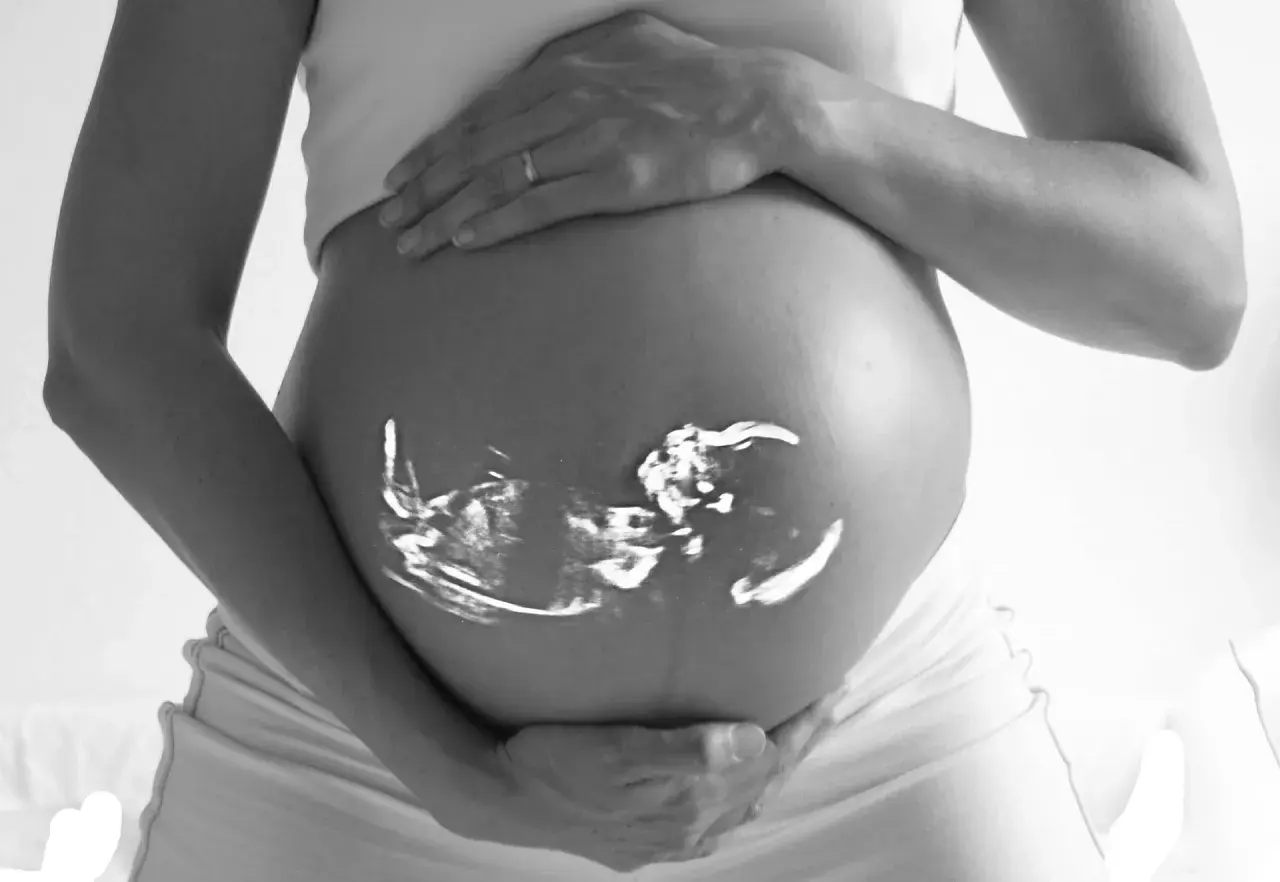 En gravid mage med ett tidigt ultraljud av ett foster projicerat på huden. Händerna vilar mjukt på magen.