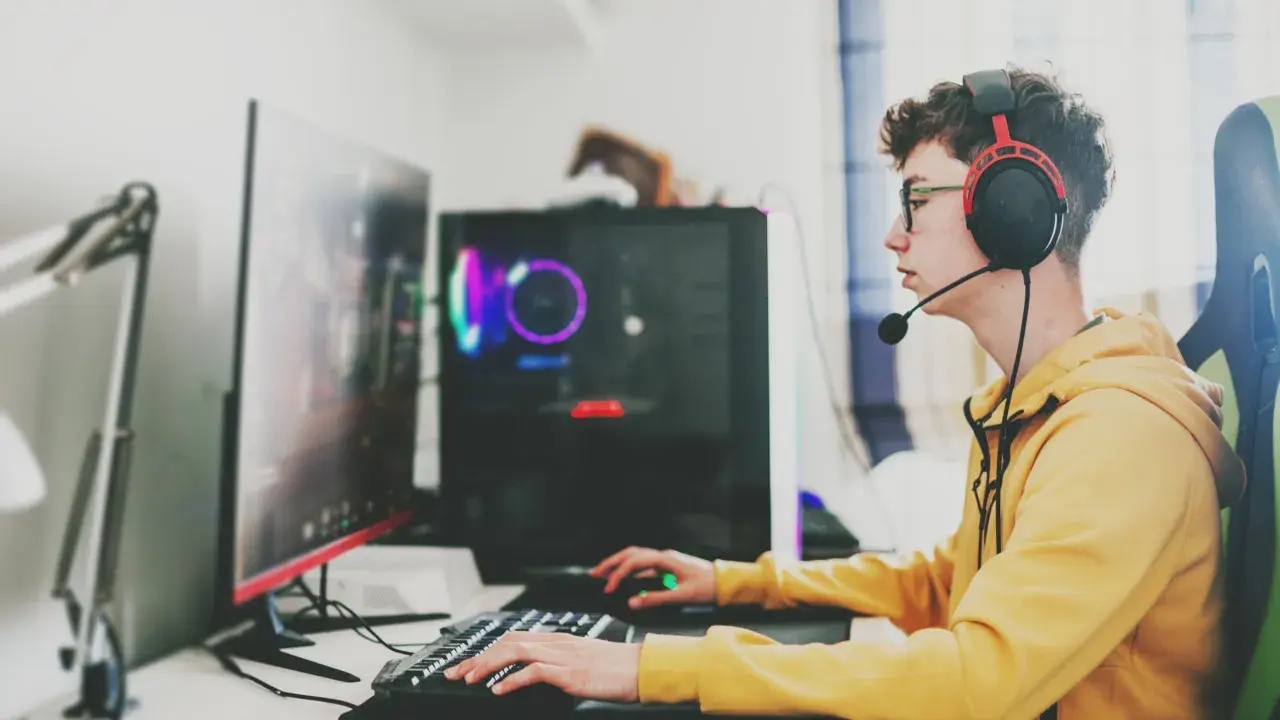 Ein junger Mann mit Kopfhörern und Brille spielt konzentriert am Computer. Sein **Computer sucht** nach neuen Herausforderungen, während er mit Tastatur und Maus agiert.