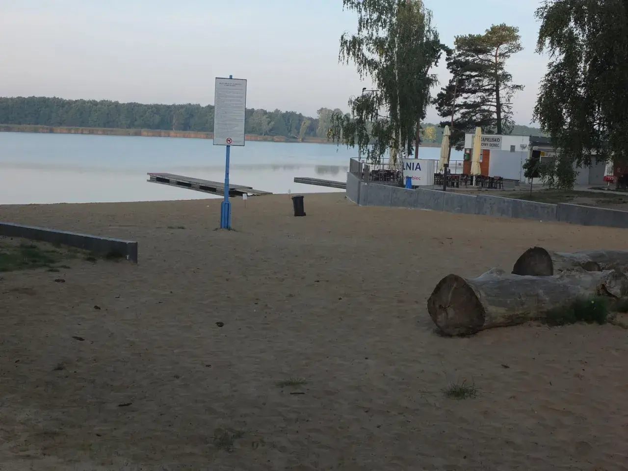 Plaża nad jeziorem Wonieść z pomostami, budynkiem kąpieliska i leżakami.