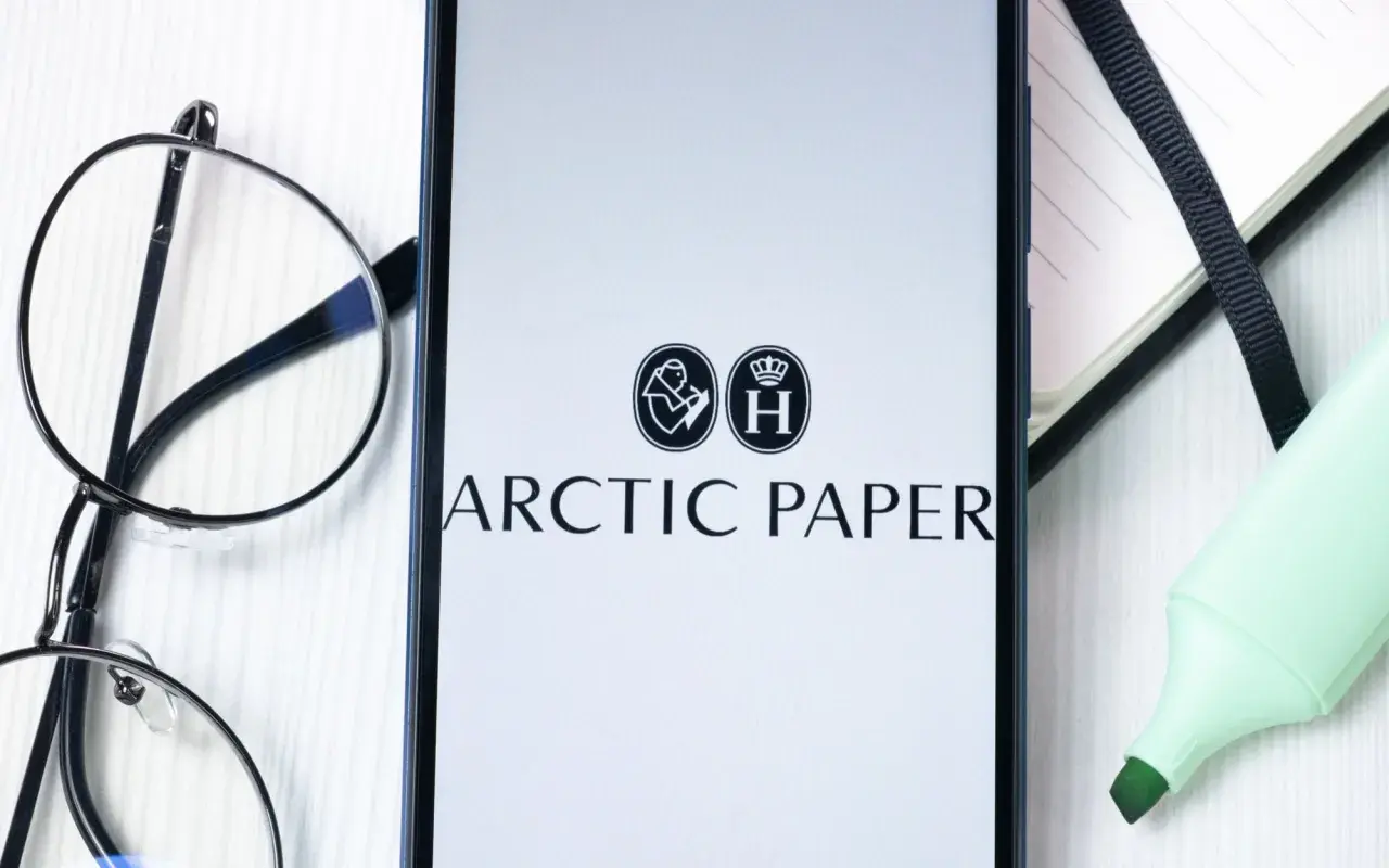 Na ekranie telefonu widnieje logo Arctic Paper. Obok leżą okulary i zielony zakreślacz, sugerując analizę akcji.