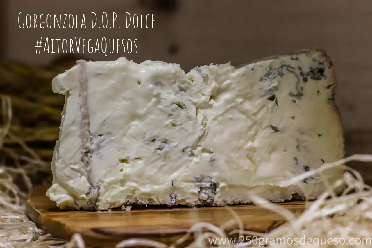 Un trozo de gorgonzola D.O.P. Dolce, un queso azul cremoso con vetas verdes y azules, sobre una tabla de madera.