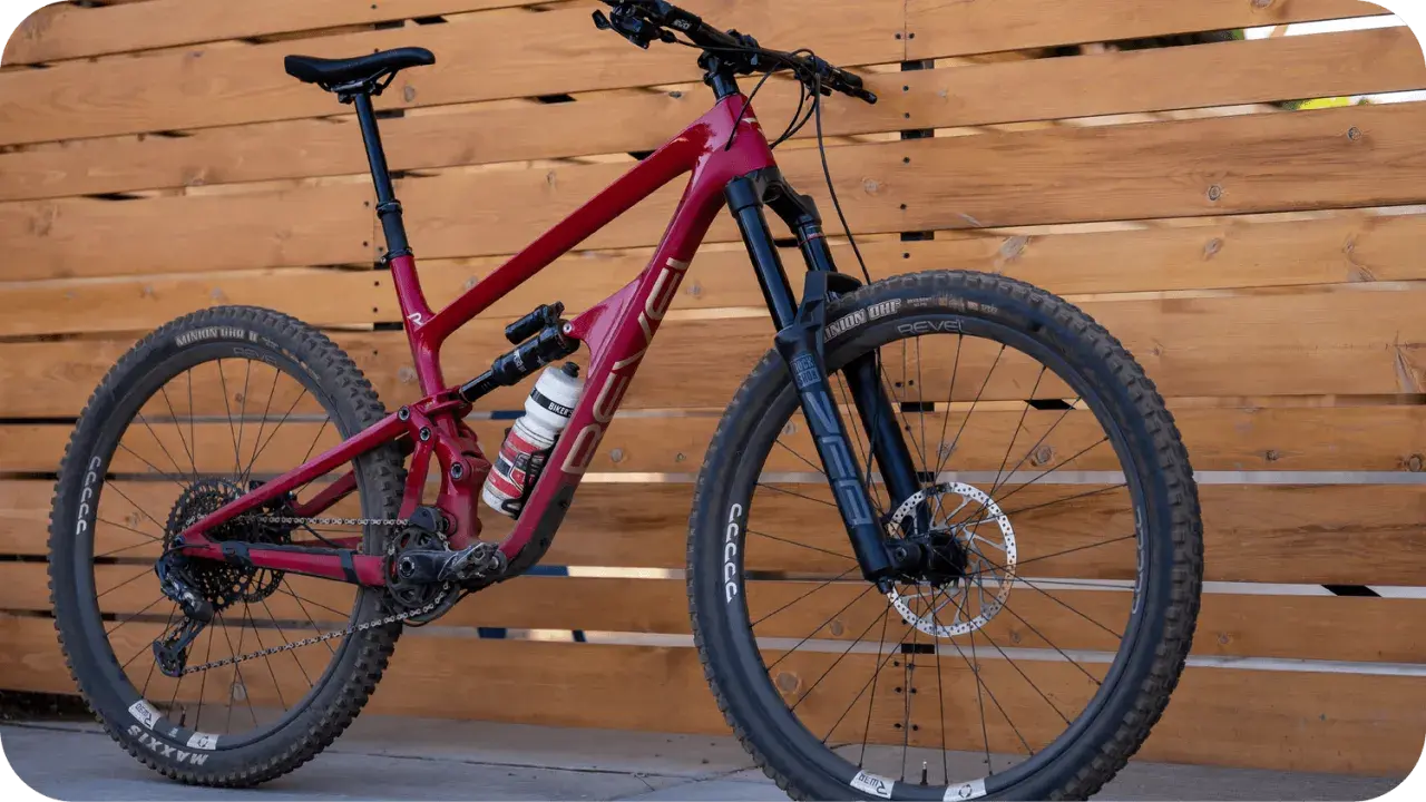 A red Revel Rail mountain bike with a water bottle, parked against a wooden fence.